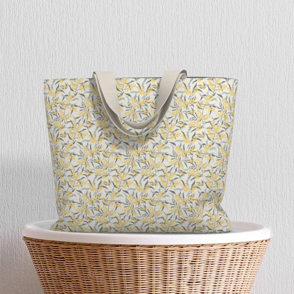 Oversized Fully Lined Cotton Tote Bag with sturdy 1 ½ inch strap. Floral botanical pattern featuring sage green leaves and yellow blossoms on a creamy white background. Shown on wicker basket.