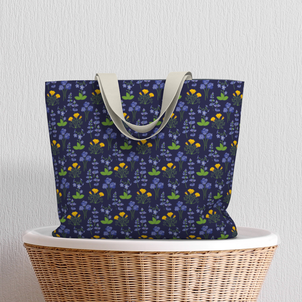 Oversized Fully Lined Cotton Tote Bag with sturdy 1 ½ inch strap. Wildflower pattern featuring California poppies and wild lupine on dark blue background. Shown on wicker basket.