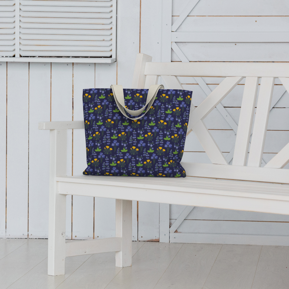 Oversized Fully Lined Cotton Tote Bag with sturdy 1 ½ inch strap. Wildflower pattern featuring California poppies and wild lupine on dark blue background. Shown on white bench.