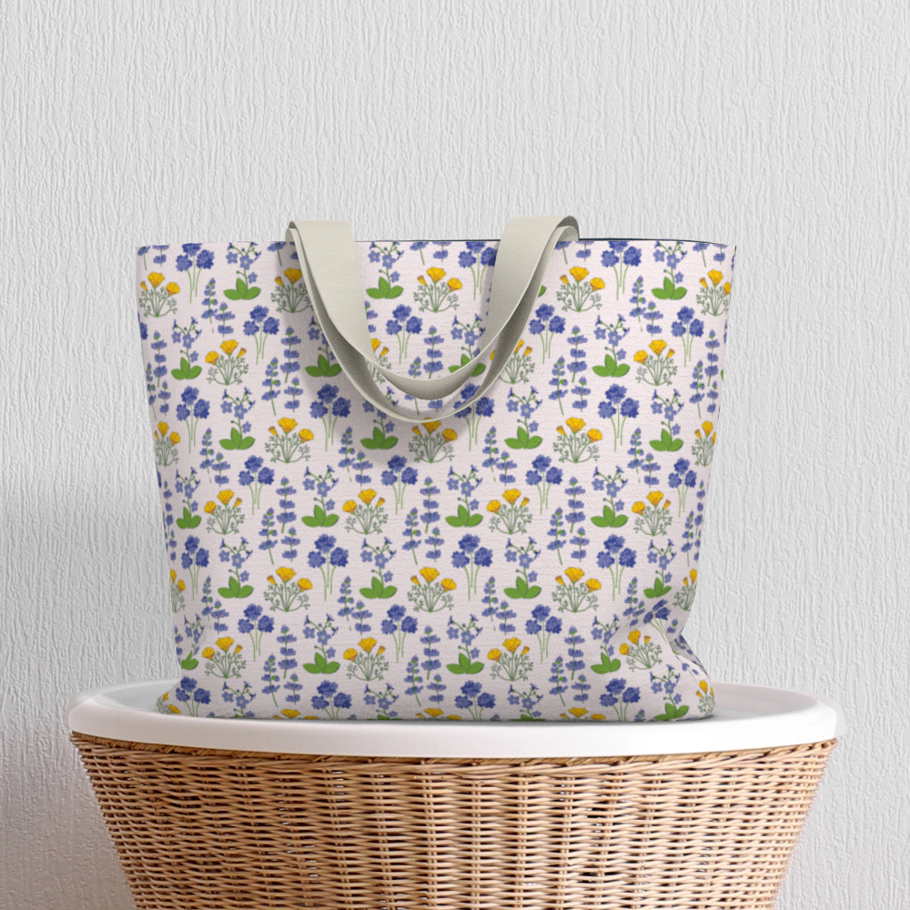 Oversized Fully Lined Cotton Tote Bag with sturdy 1 ½ inch strap. Wildflower pattern featuring California poppies and wild lupine on light pink background. Shown on wicker basket.