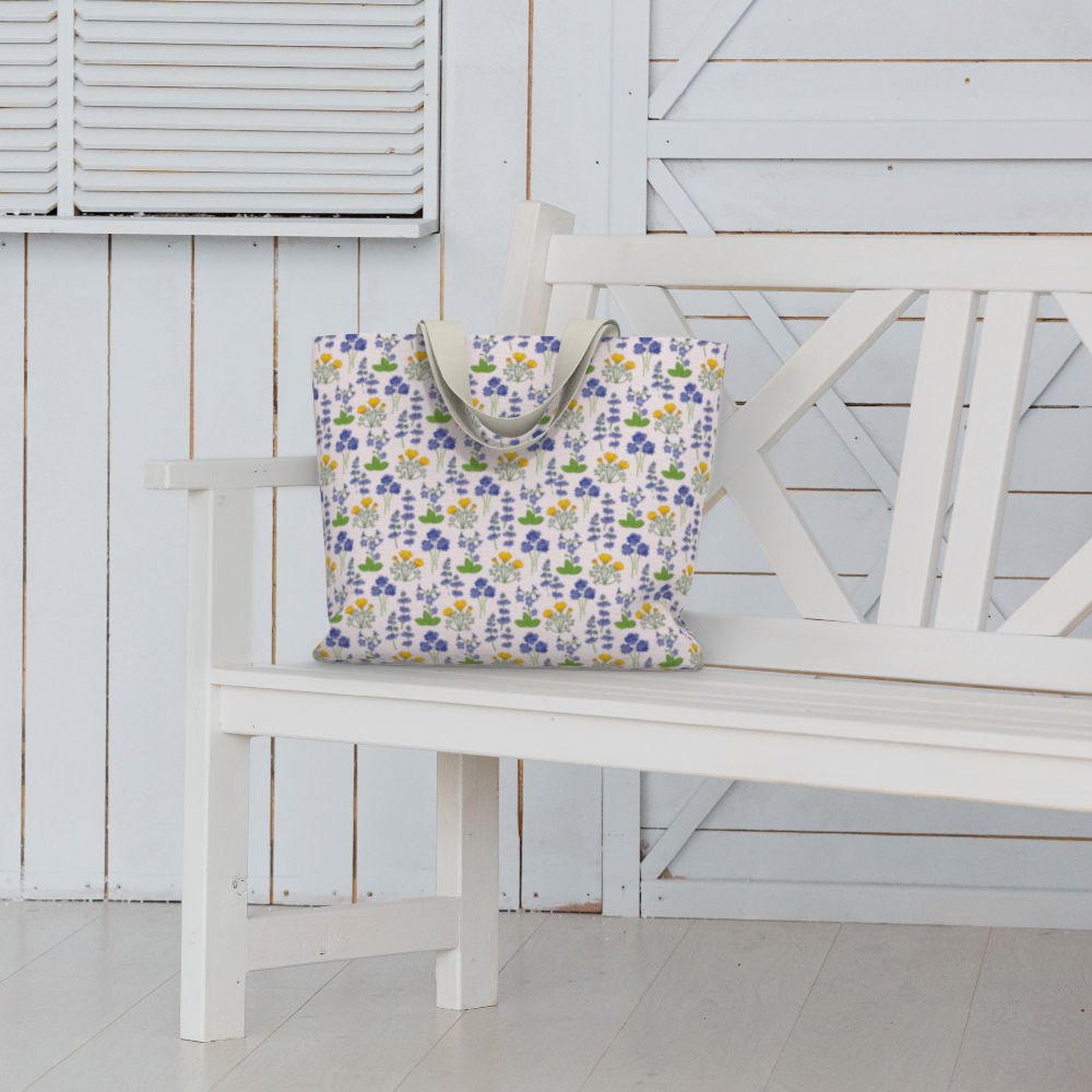 Oversized Fully Lined Cotton Tote Bag with sturdy 1 ½ inch strap. Wildflower pattern featuring California poppies and wild lupine on light pink background. Shown on white bench.